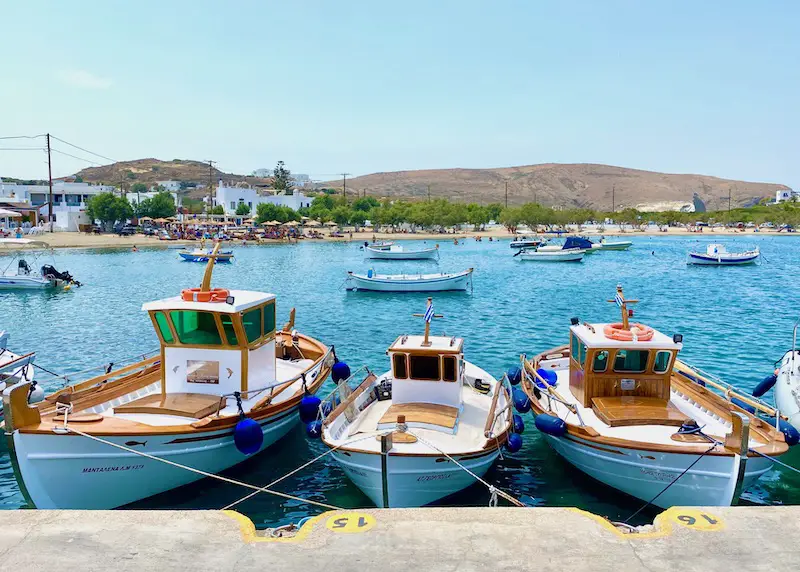 Où séjourner à Milos en 2023 ? 14 Bateaux de pêche à la jetée avec la plage de Pollonia en arrière-plan