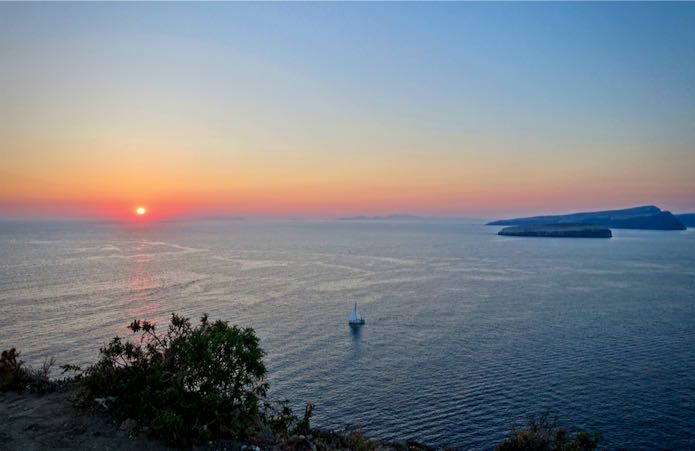 Coucher de soleil sur la mer Égée avec un voilier et le volcan de Santorin en vue.